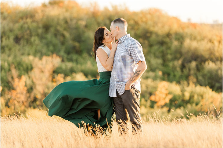 man and woman kissing in grass with wind blowing skirt