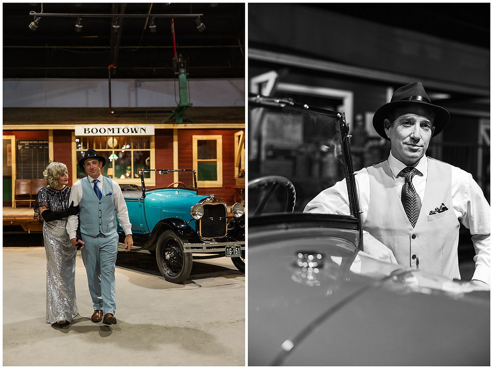 Couple in 1920s attire walks by teal vintage car; backdrop reads "Boomtown." Man in vest leans on car. Retro setting, nostalgic mood.