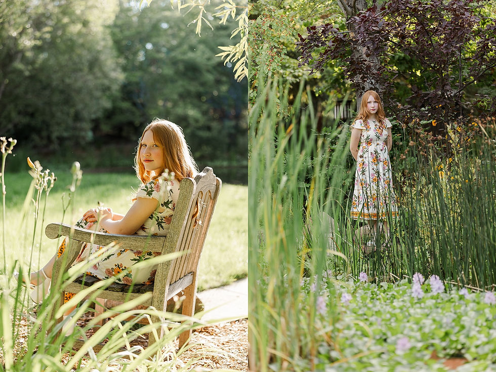 Woman in a floral dress sits on a wooden bench in a sunlit garden. She stands among tall plants, with lush greenery and purple flowers in view.