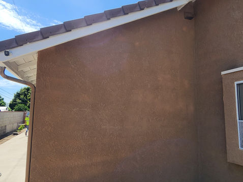 Brown stucco wall with a window and roof tiles.