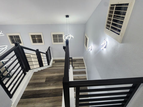 Modern staircase with dark railings and wall lights.