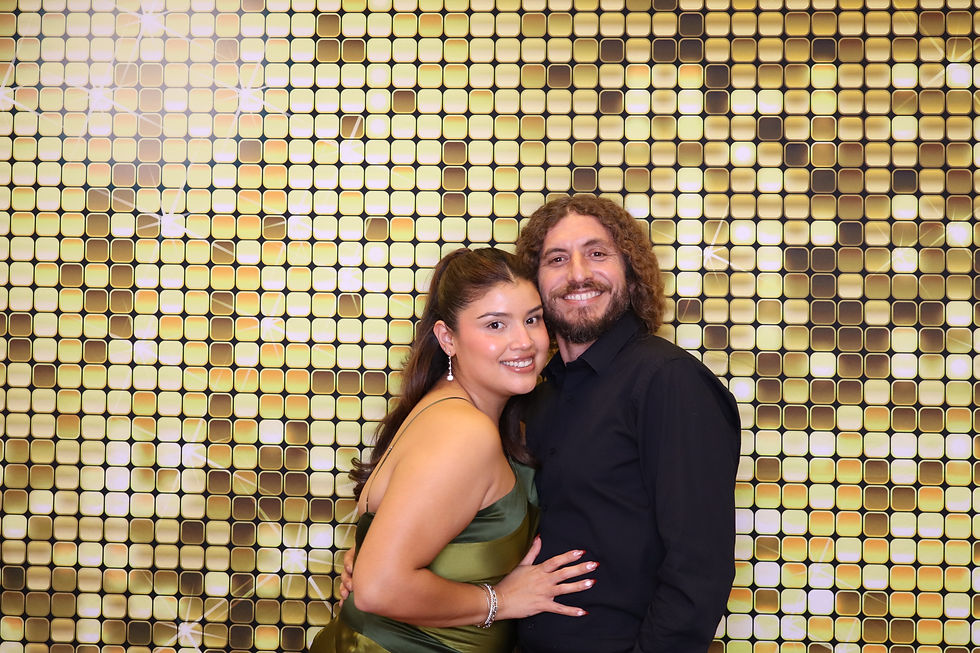 Couple posing at an Events Squad photo booth with a gold sequin backdrop, dressed in formal evening attire and smiling.