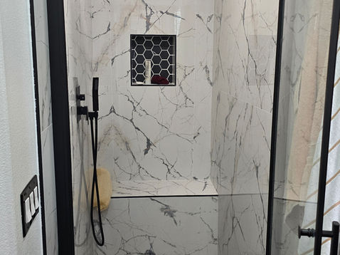 Modern shower with marble walls and black fixtures.
