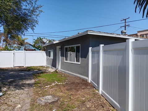 Gray house with white fence and blue sky.