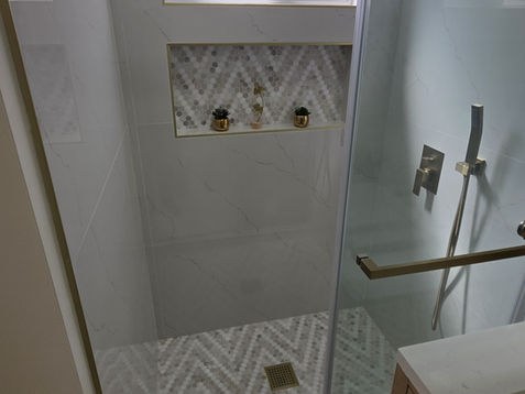Small modern shower with glass door and patterned tiles.