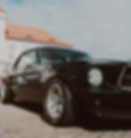 Classic black Ford Mustang parked beside elegant architecture in natural daylight.
