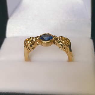 two carved lions on the shoulders of a yellow gold engagement ring holding a blue sapphire in a bezel setting in ring box
