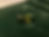 A rectangular yellow-green parti color sapphire rests on a dark green velvet surface, reflecting light.