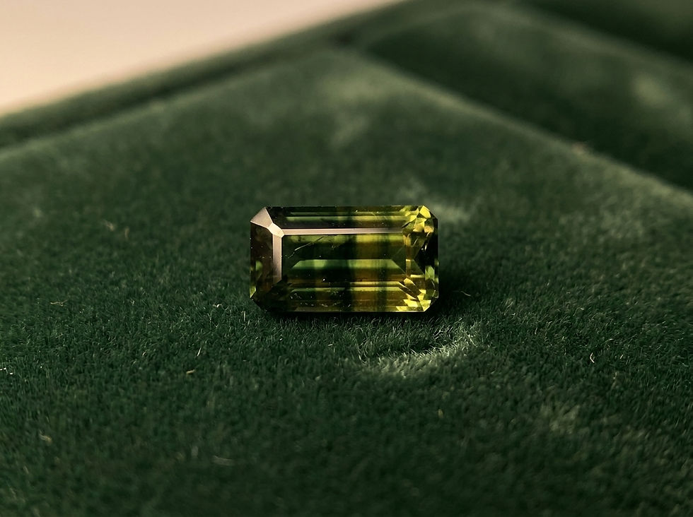 A rectangular yellow-green parti color sapphire rests on a dark green velvet surface, reflecting light.