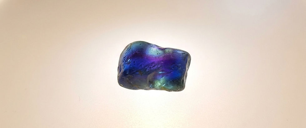 a piece of rough parti color sapphire gem on a light table, exhibiting deep cobalt blues and green patches