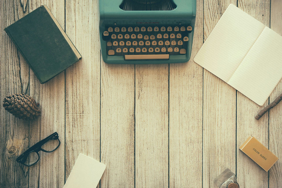 a wooden table with a type writer, book, paper, and a pair of glasses.