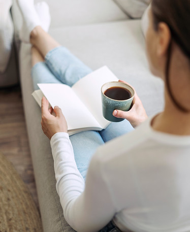 Back rear view of young woman in casual wear sit on comfortable sofa, hold coffee cup in h