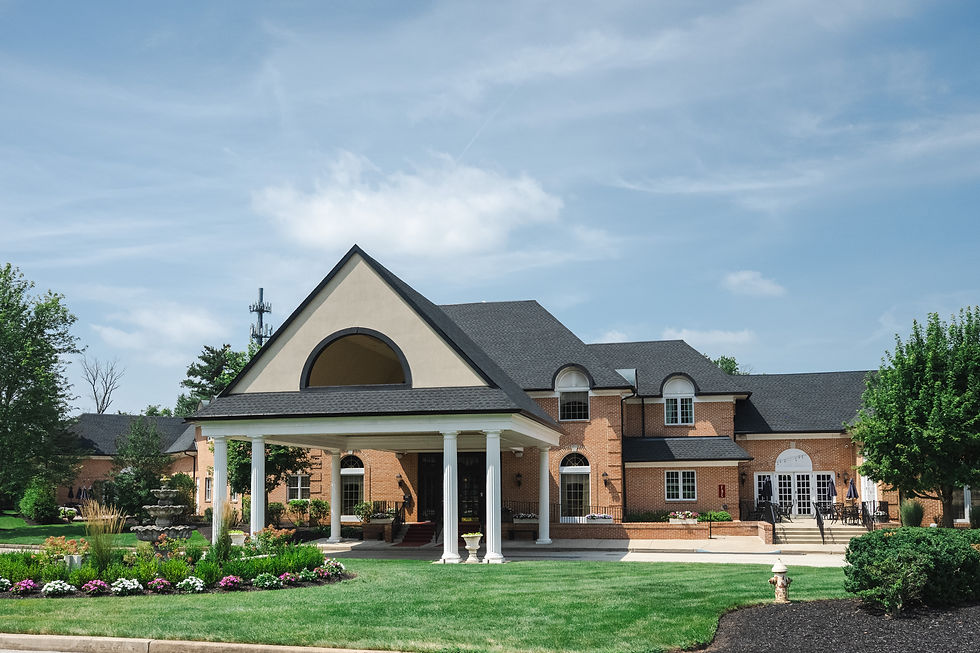 Brick building with white columns and arched windows, set in a manicured garden with colorful flowers. Clear sky enhances tranquil vibe.