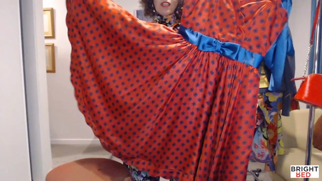 Stephanie Rumble holding up a red satin race day dress with a turquoise bow and navy print.