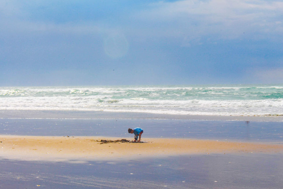 A photo with a blue tint of a boy on a sand bar at a beach.