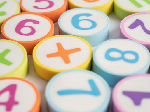 Colorful plastic number tiles with digits and plus sign scattered on a white background, like a playful math set