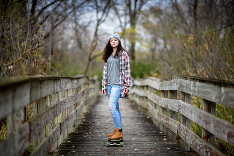 Graduation portrait of a girl riding her skateboard over a wooden bridge