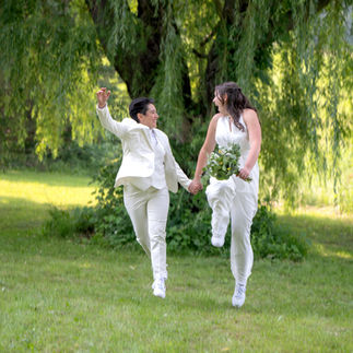 A joyful moment from a same-sex micro wedding, featuring a couple in elegant attire. They are surrounded by intimate, natural settings or a small, personal ceremony setup. The focus is on the couple's connection and love, with soft lighting highlighting the intimate atmosphere