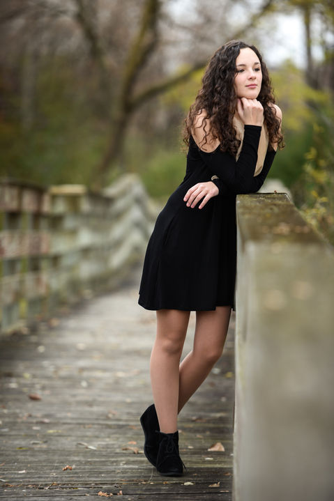 Graduation portrait of a girl leaning against an old wooden bridge