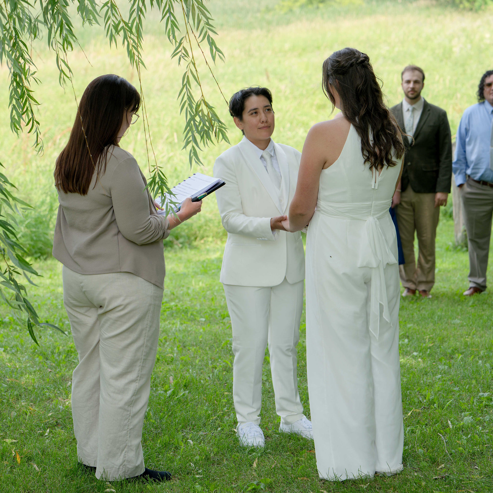 A joyful moment from a same-sex micro wedding, featuring a couple in elegant attire. They are surrounded by intimate, natural settings or a small, personal ceremony setup. The focus is on the couple's connection and love, with soft lighting highlighting the intimate atmosphere