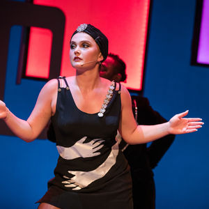 An actress wearing a black dress with white "gloves" wrapping around her