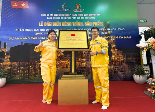 Lễ công bố: Hai người mặc đồng phục vàng bên bảng vàng.