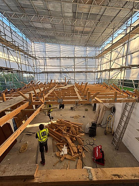 A professional home extension site in Barnet under a temporary scaffold roof, showing structural timber floor joists, organized construction materials, and a site worker in a high-visibility vest.