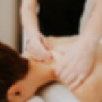 Person receiving shoulder massage in a bright room. Hands applying pressure on shoulder. Relaxing mood, no text visible.