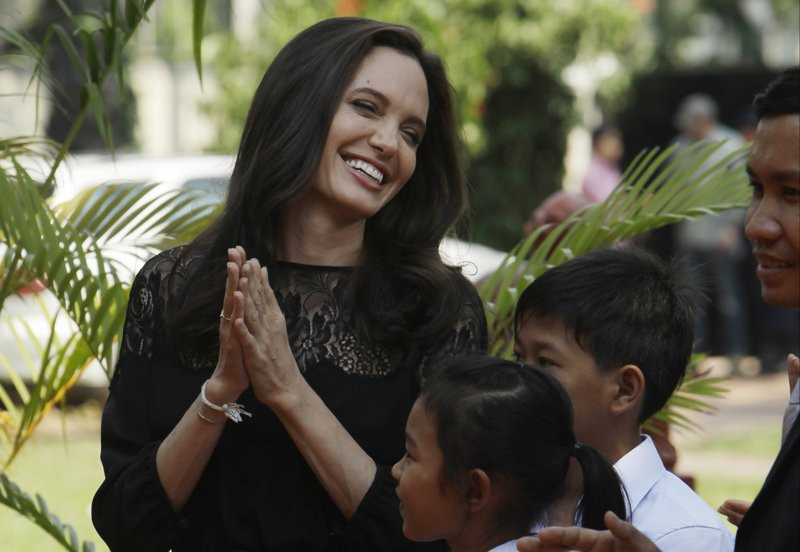 Angelina Jolie de mãos dadas e sorrindo ao redor de crianças no Cambodia