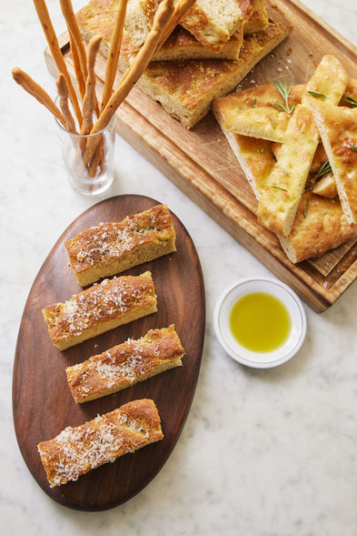 Focaccia bread with breadsticks, olive oil and rosemary on wooden boards.