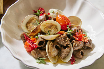 Pasta dish with clams, tomatoes, and herbs served in a white bowl