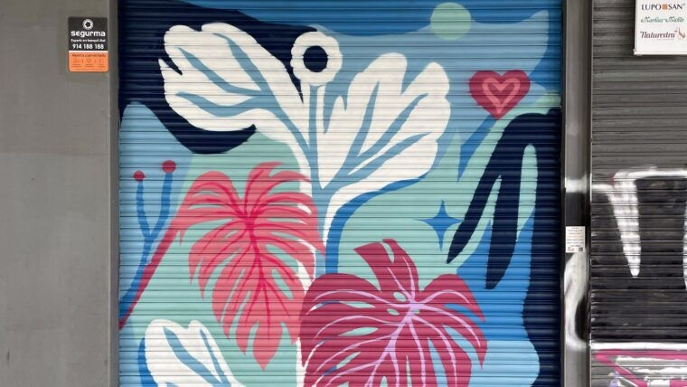 Mural colorit sobre una persiana metàl·lica amb fulles blanques i roses, un cor i rètols a banda i banda.
