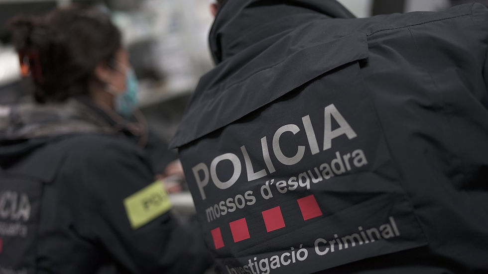 Agents dels Mossos d'Esquadra en uniforme negre amb la inscripció "POLICIA". Un agent porta mascareta. Escena a l'interior, ambient seriós.