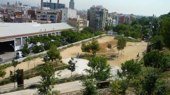 Parc urbà amb camins, arbres i edificis al fons en un dia clar i assolellat.