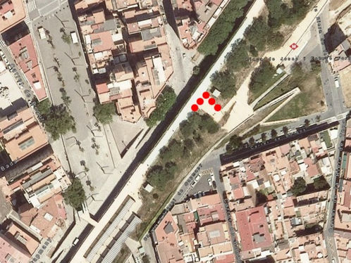 Vista aèria d'un barri urbà amb edificis i carrers estrets. Una línia de punts vermells destaca en un camí, envoltat per arbres i zones verdes.