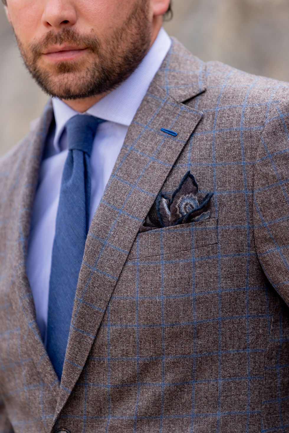 Man wearing a checked jacket, blue shirt and tie, and pocket square.