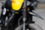Close-up of a yellow motorcycle's front, showing the headlight and black suspension. The brand name "BSA" is visible on the tank.