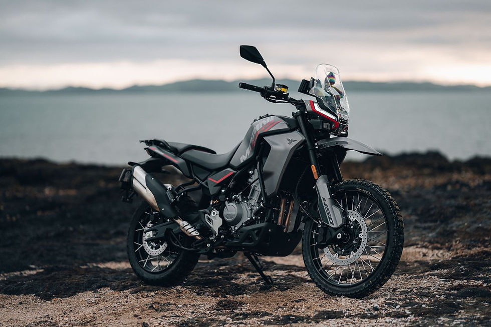 Black and gray adventure motorcycle parked on a rocky shoreline with calm sea and cloudy sky, creating a moody outdoor scene.