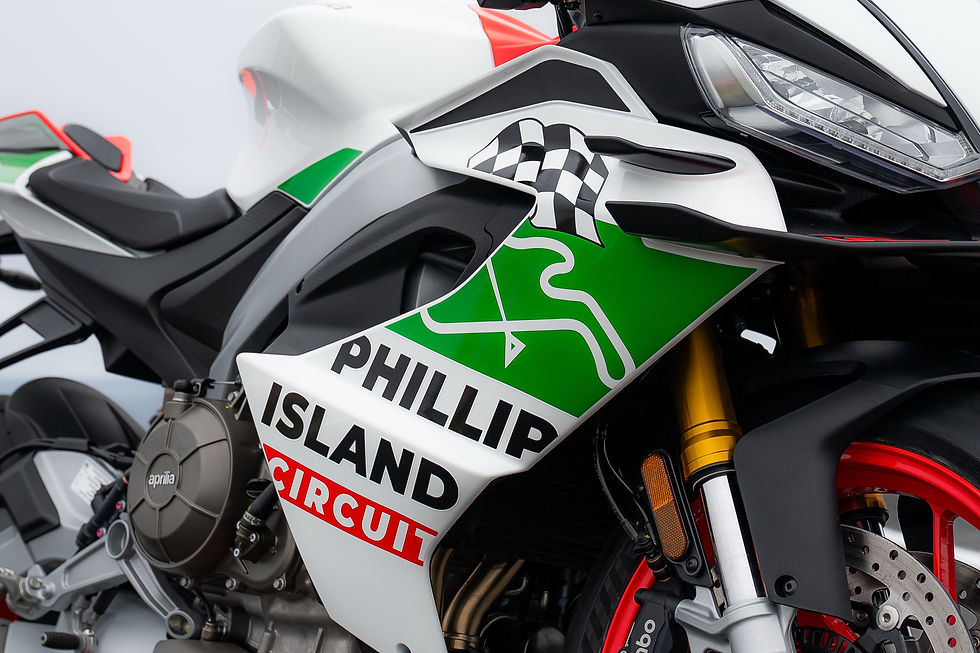 Close-up of an Aprilia sport motorcycle with green, white and black racing livery, PHILLIP ISLAND CIRCUIT text, studio background.