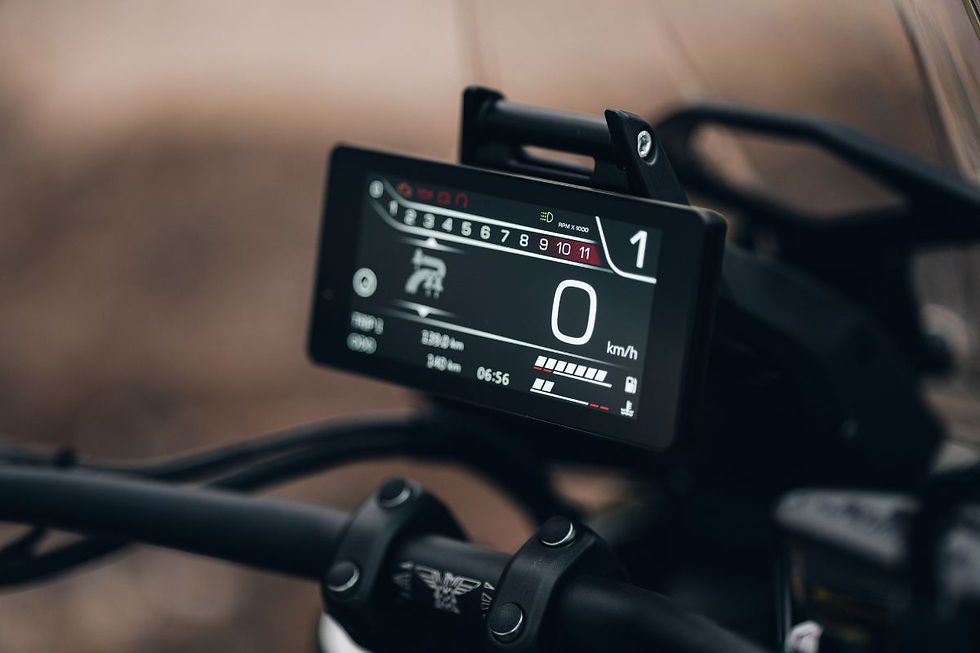 Close-up of a motorcycle digital dash on handlebars, showing 0 km/h in first gear against a blurred road.