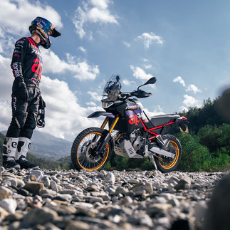Man stands in front of motorcycle in a riverbed