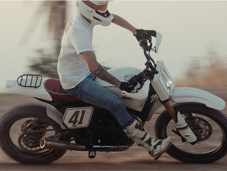 A white motorcycle being ridden by a guy in blue jeans and a t shirt