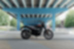 A black motorcycle under a blue bridge with greenery and urban elements in the background. BSA logo visible on the bike.