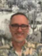 Smiling man wearing glasses, desert-themed backdrop