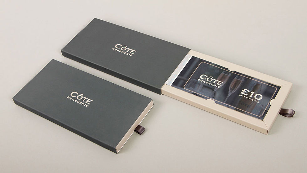A grey and tan sliding box
with Cote logo holding a
paper gift voucher