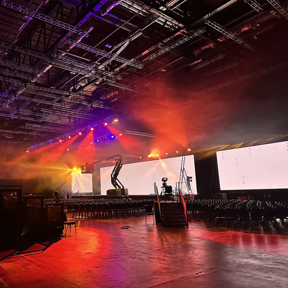 Large event hall with stage and screens brightly lit with colorful lights.