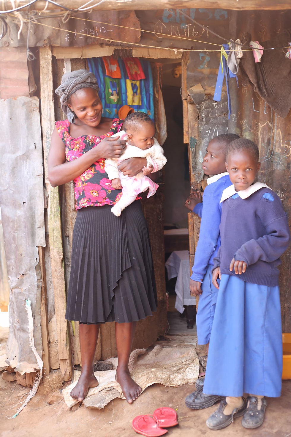 Mother holding baby, with children in uniform visible at the doorway.