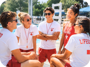 Group of lifeguards gathered poolside at an outdoor aquatic facility, smiling and talking together during a team break on a sunny day.