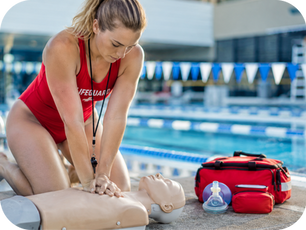 Lifeguard practicing CPR on a training manikin beside an indoor swimming pool during aquatic safety training.