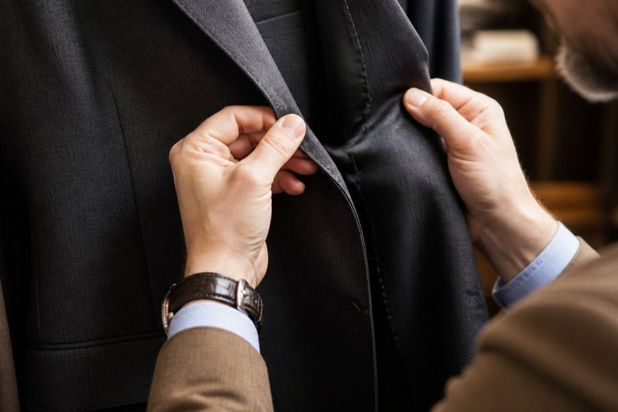 Close-up of a man's hands examining the stitching and seam quality of a tailored blazer in a well-lit room